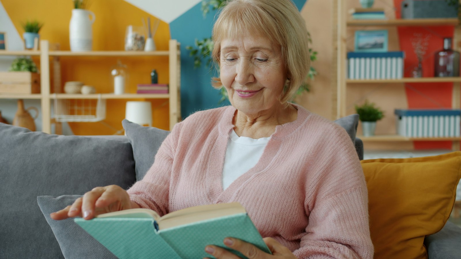 Woman in a pink cardigan reading a book at home